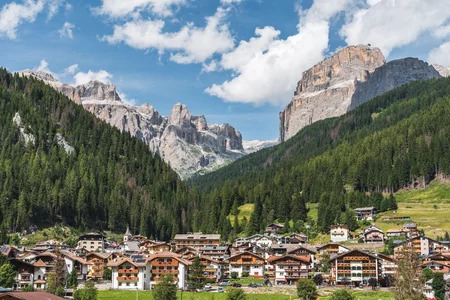 Un paese della Val di Fassa con case tipiche e uno sfondo mozzafiato delle montagne, in una splendida giornata estiva
